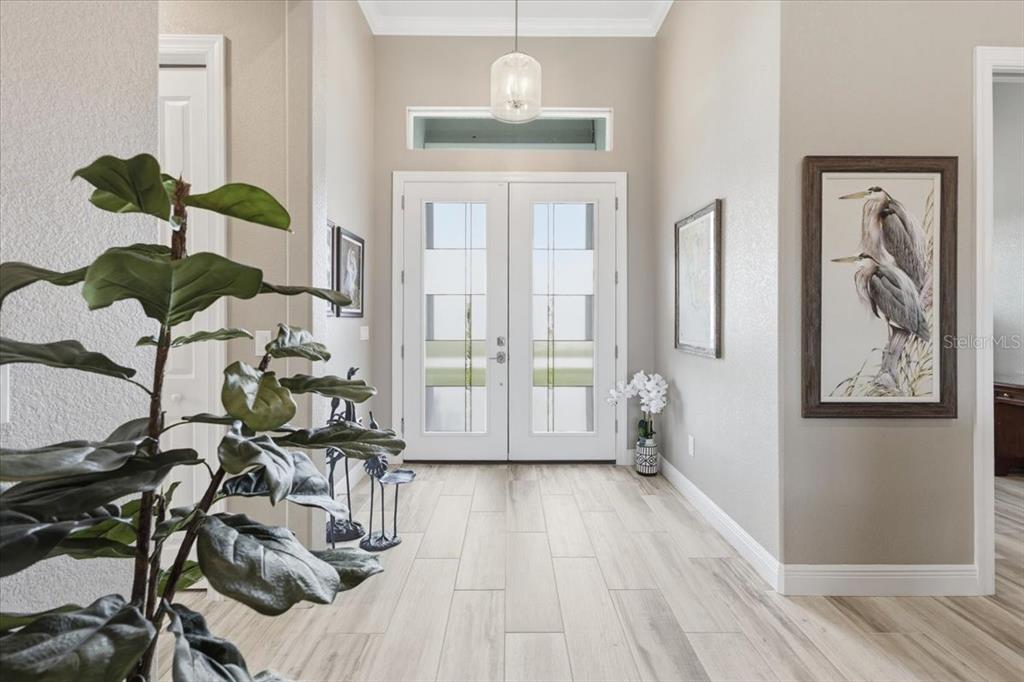 A bright entryway features double glass-paneled doors, light wood-look tile flooring, and a pendant light — 9214 MELODY CIRCLE, PORT CHARLOTTE, FL