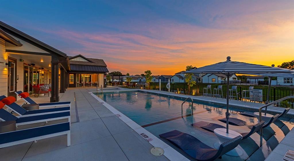 A swimming pool with lounge chairs and an umbrella at sunset next to a building — 4980 RED MAPLE LANE UNIT B1, WILDWOOD, FL