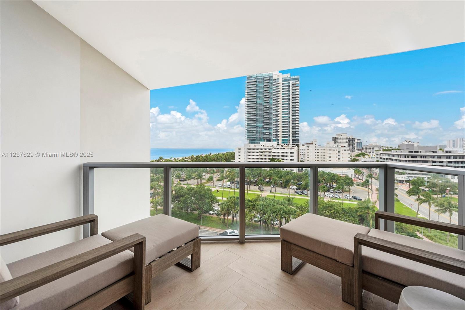A balcony with two wooden lounge chairs overlooks a park, city buildings, and the ocean — 2201 Collins Ave # 804, Miami Beach FL 33139, MIAMI BEACH, FL
