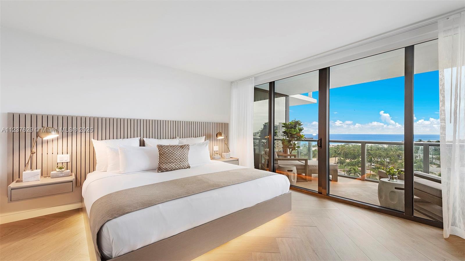 A modern bedroom features a slatted wood headboard, platform bed, and floor-to-ceiling windows overlooking the ocean — 2201 Collins Ave # 804, Miami Beach FL 33139, MIAMI BEACH, FL