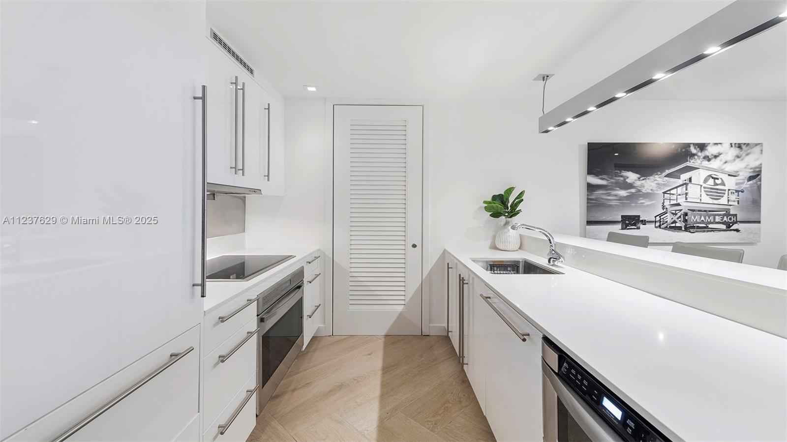 A modern white galley kitchen features stainless steel appliances, quartz countertops, and light wood flooring — 2201 Collins Ave # 804, Miami Beach FL 33139, MIAMI BEACH, FL
