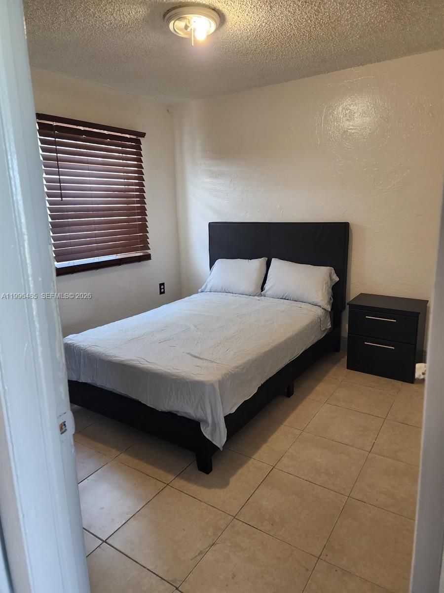 A bedroom features a black bed frame, a matching nightstand, and tile flooring — 715 NW 7th Ave # 4, Hallandale Beach FL 33009, HALLANDALE BEACH, FL