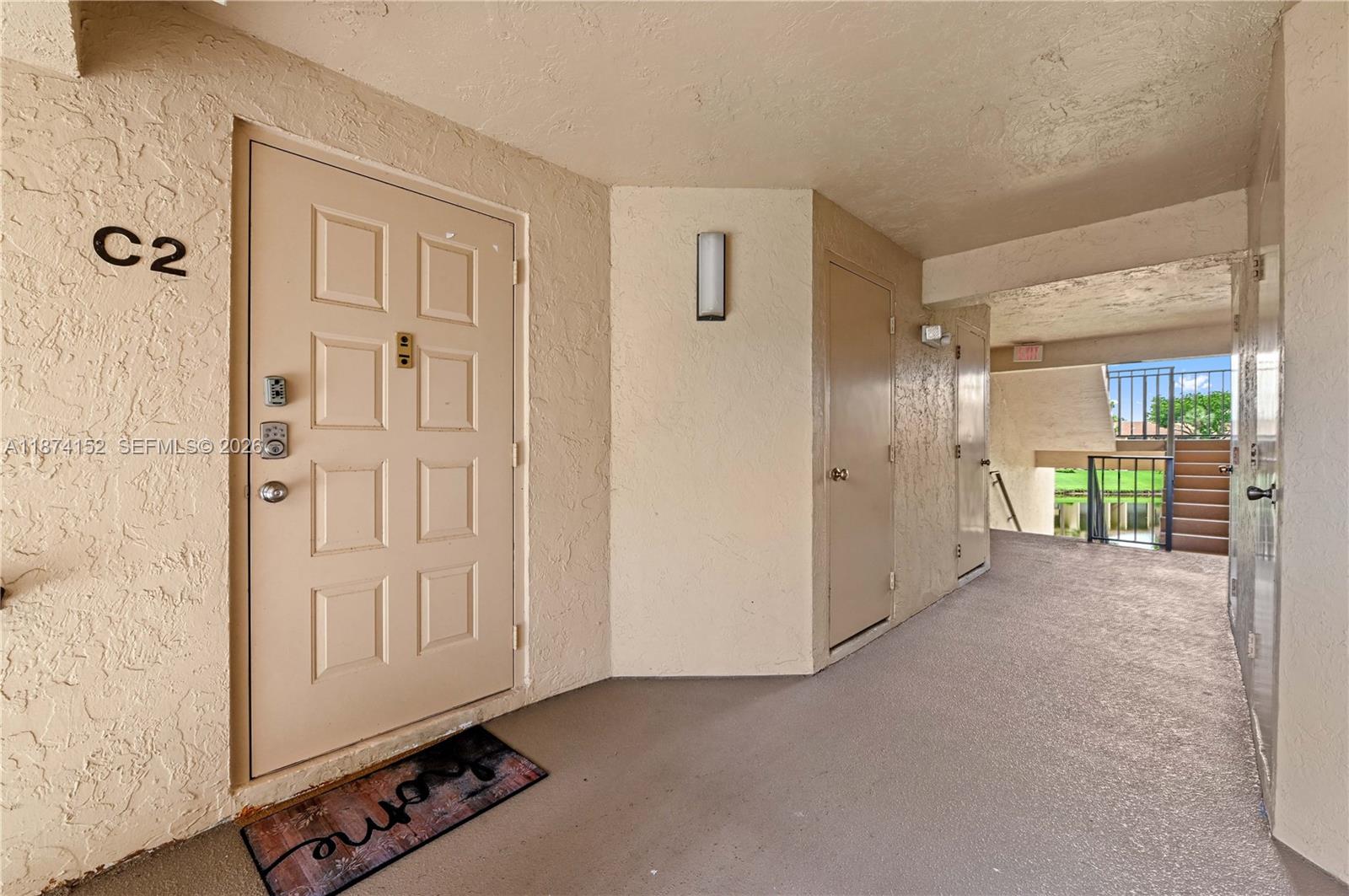This exterior hallway shows apartment unit C2 with a beige door and a welcome mat — 812 Sky Pine Way # C2, Green Acres FL 33415, GREEN ACRES, FL