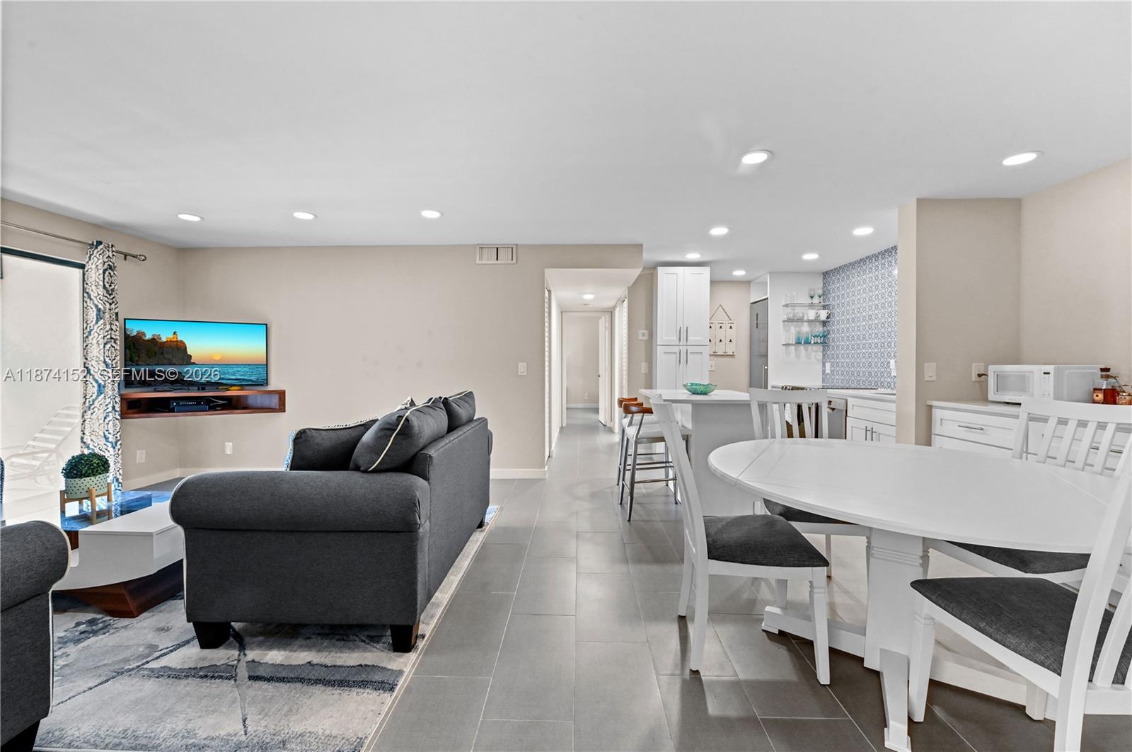 An open-concept living and dining area features gray tile flooring, a dark sofa, and white cabinetry — 812 Sky Pine Way # C2, Green Acres FL 33415, GREEN ACRES, FL