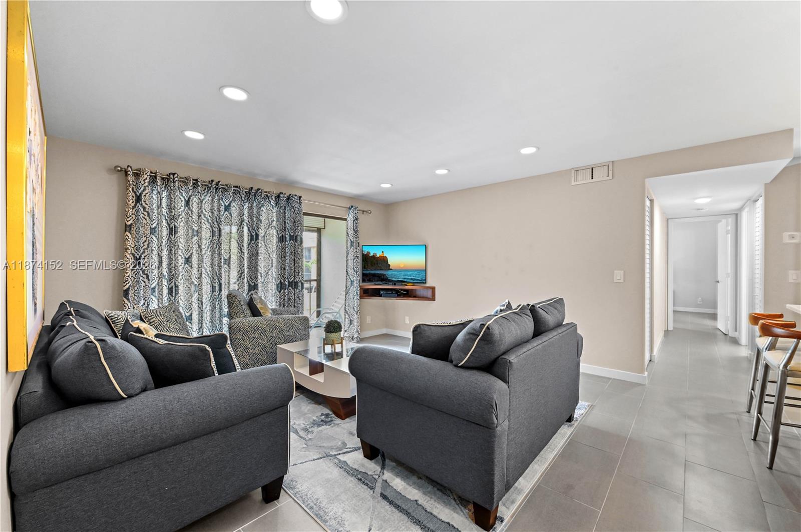 A living room features gray sofas, a patterned rug, and a wall-mounted television — 812 Sky Pine Way # C2, Green Acres FL 33415, GREEN ACRES, FL