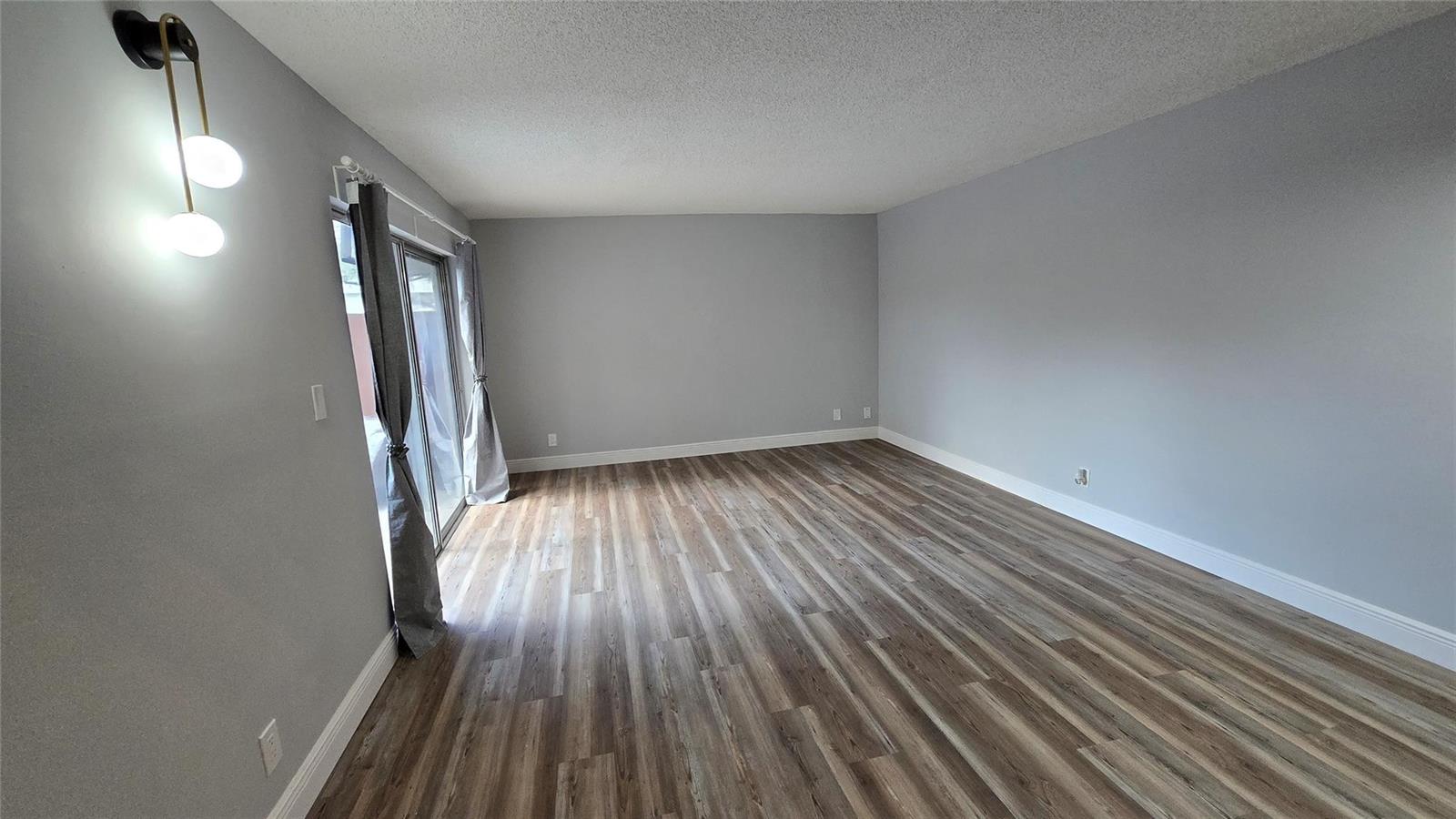 An empty room features gray walls, wood-look flooring, and a sliding glass door with curtains — 8900 SW 20th Place # A, Davie FL 33324, DAVIE, FL