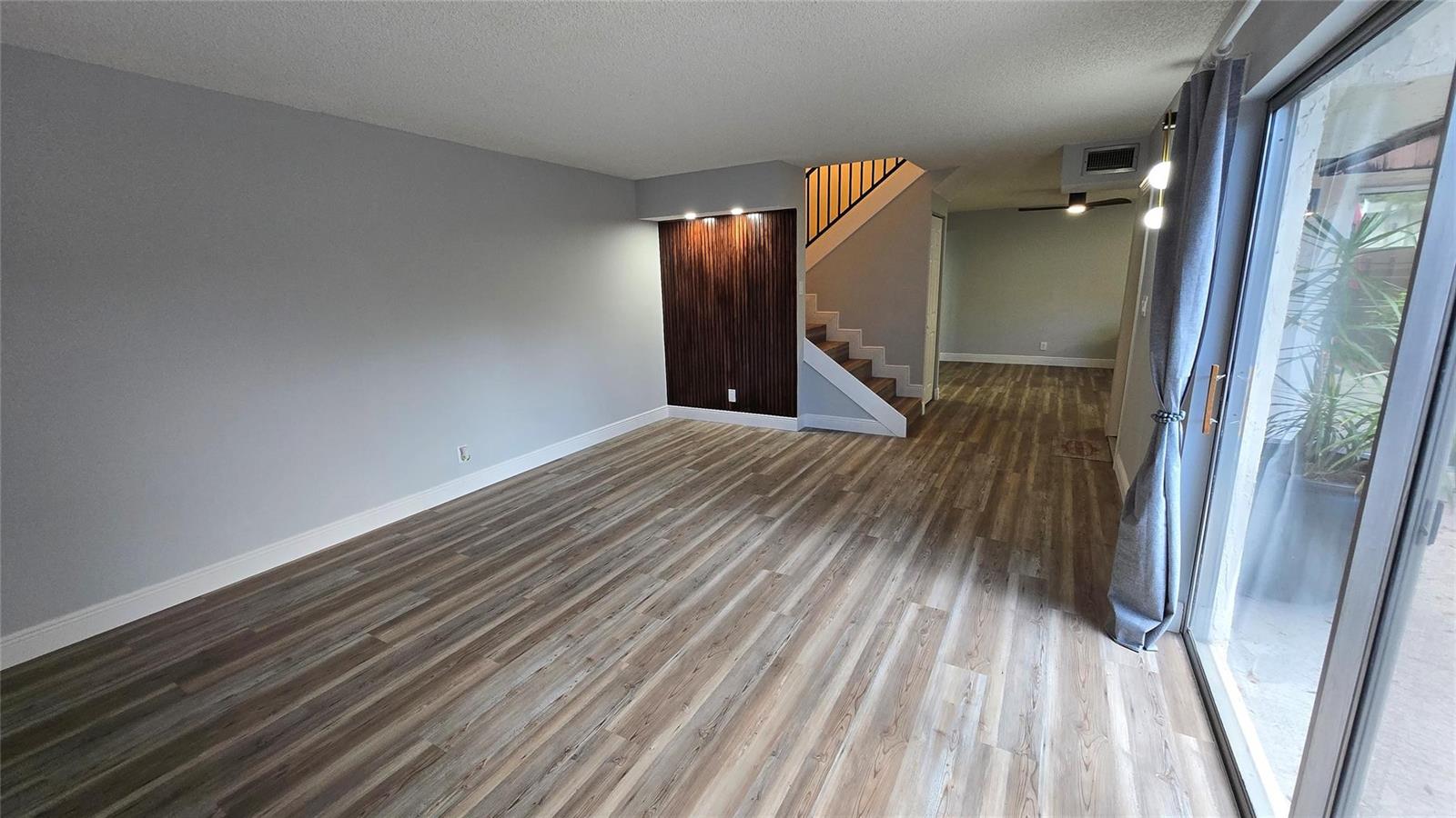 An empty living room features wood-look flooring, a wood-slat accent wall, and a staircase — 8900 SW 20th Place # A, Davie FL 33324, DAVIE, FL