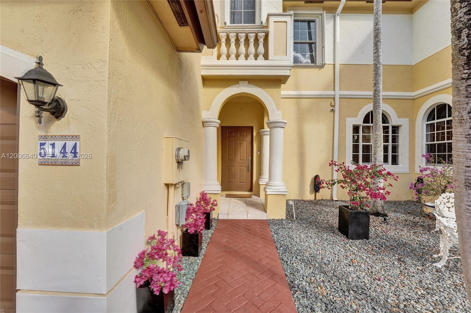 The exterior of a yellow house features a brick walkway, arched entryway, and potted bougainvillea — 5144 SW 141st Ter, Miramar FL 33027, MIRAMAR, FL