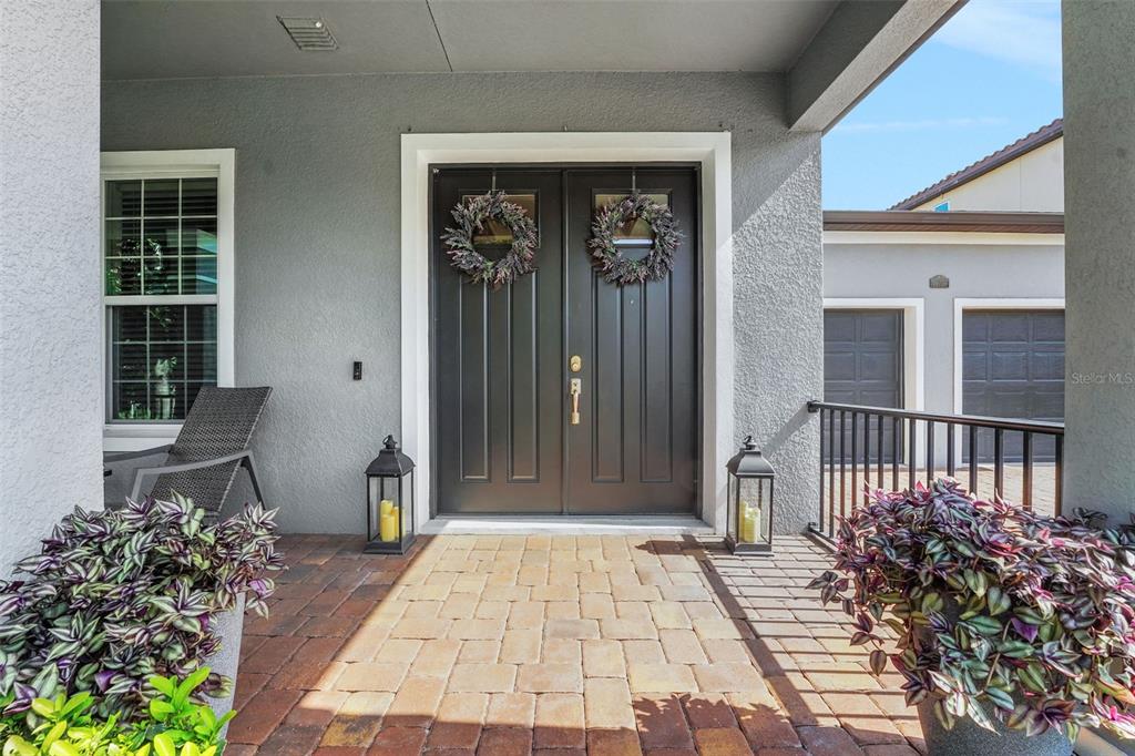 A covered front porch features a double door entry, brick pavers, and potted plants — 16736 GULLFLOSS TERRACE, WINTER GARDEN, FL