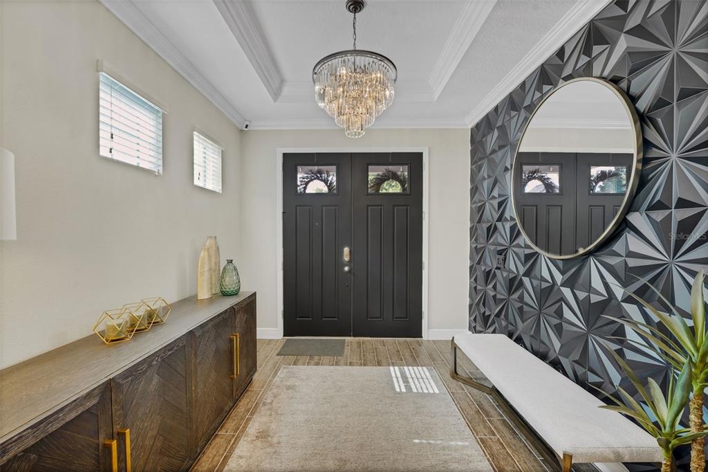 A modern entryway features a black double door, a crystal chandelier, and a geometric accent wall — 16736 GULLFLOSS TERRACE, WINTER GARDEN, FL