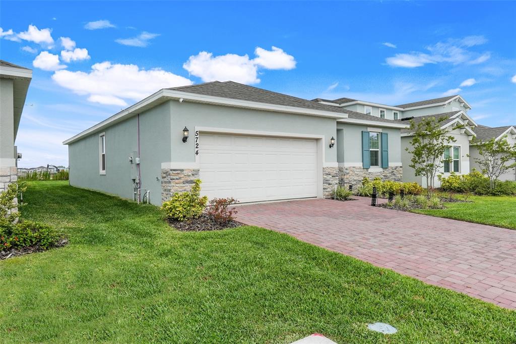 A light green house with a two-car garage, stone accents, and a brick paver driveway — 5724 CAMILLA STREET, ST CLOUD, FL