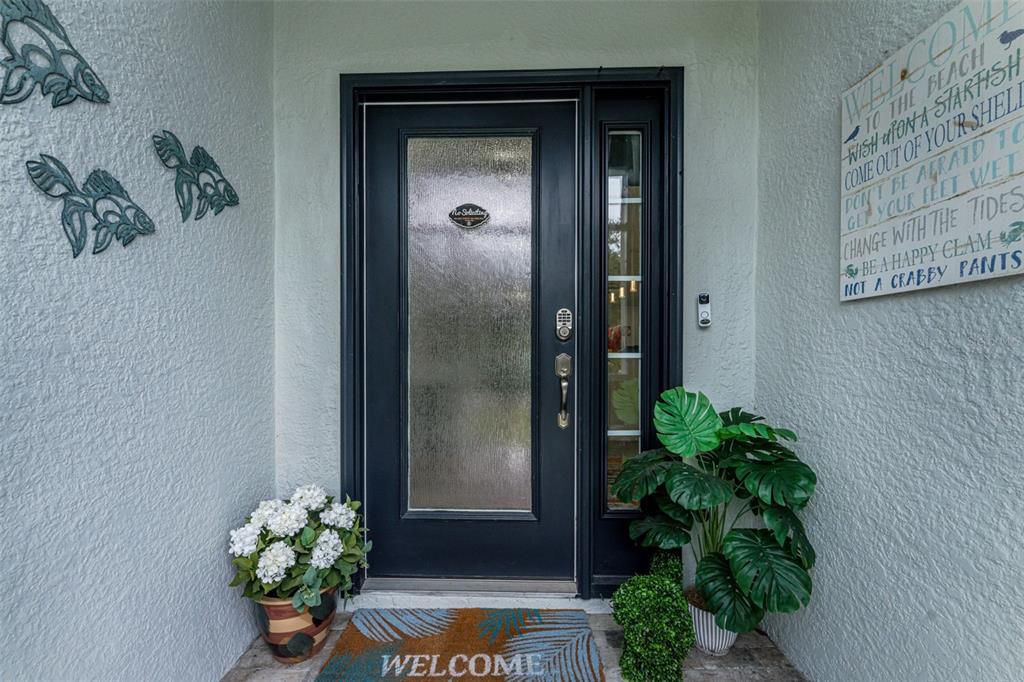 A front entrance features a dark door with a sidelight, potted plants, and wall decor — 10177 WILDCAT STREET, PORT CHARLOTTE, FL