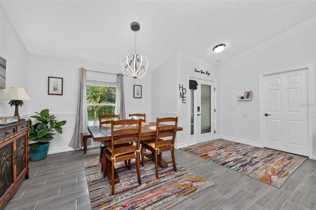 A dining room features a wooden table, chairs, a modern chandelier, and gray tile flooring — 10177 WILDCAT STREET, PORT CHARLOTTE, FL