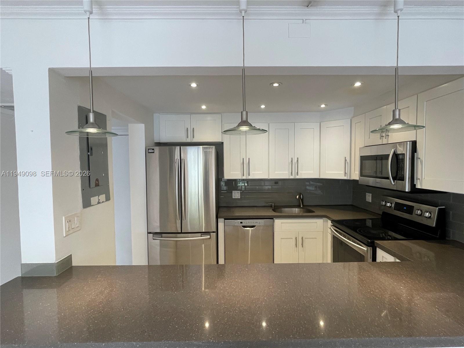 A kitchen features white cabinets, stainless steel appliances, and a dark stone countertop peninsula — 1650 NE 115th St # 311, Miami FL 33181, MIAMI, FL