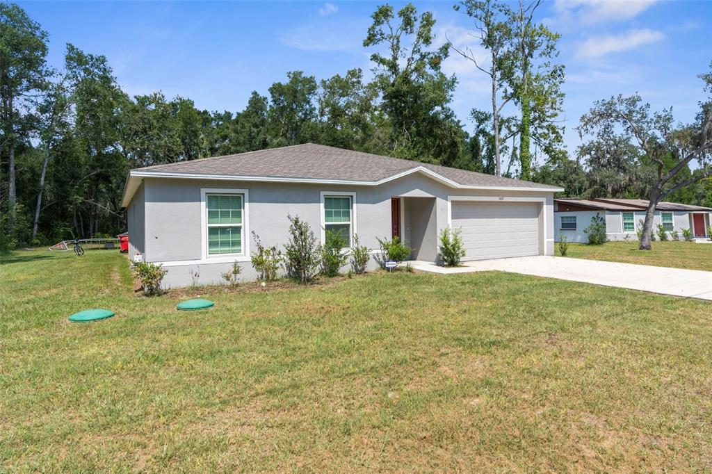 A single-story gray house with a two-car garage sits on a grassy lot — 5637 E TANGELO LANE, INVERNESS, FL