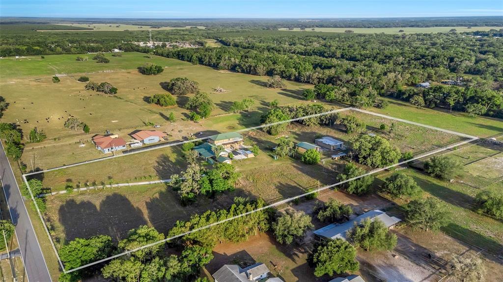 An aerial view shows a rural property with multiple buildings, fenced pastures, and surrounding trees — 20138 BOWMAN ROAD, SPRING HILL, FL
