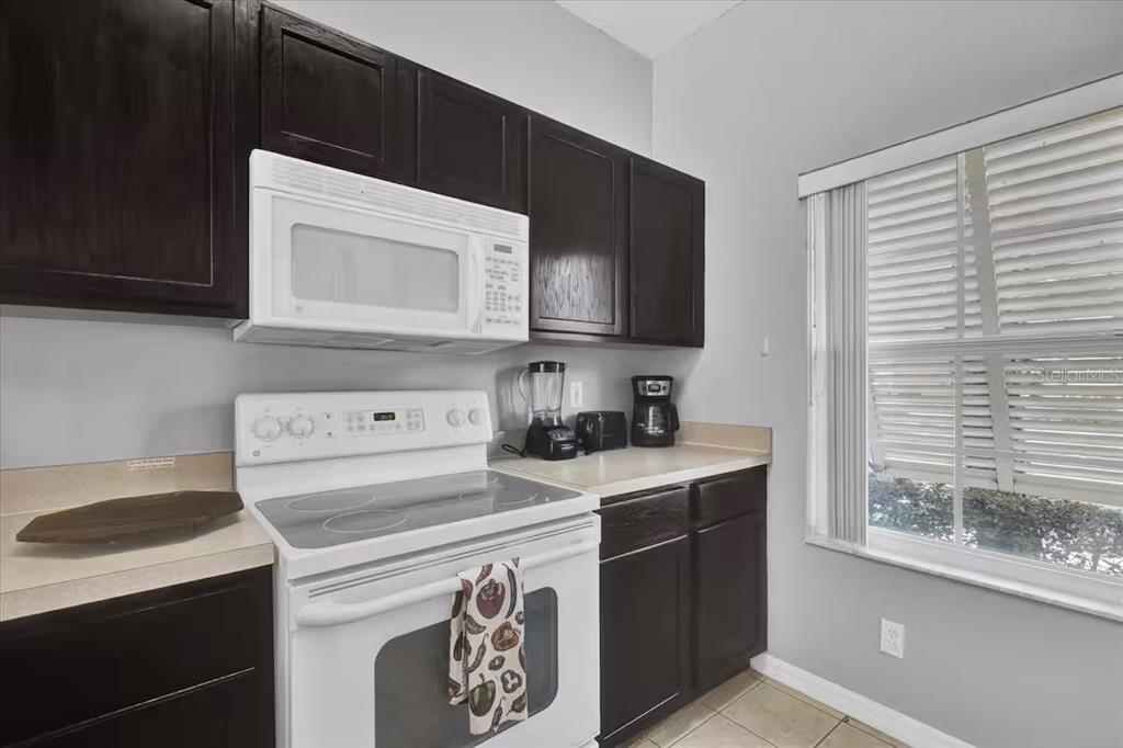 A kitchen features dark wood cabinets, white appliances, a light countertop, and a window — 8515 CRYSTAL COVE LOOP, KISSIMMEE, FL