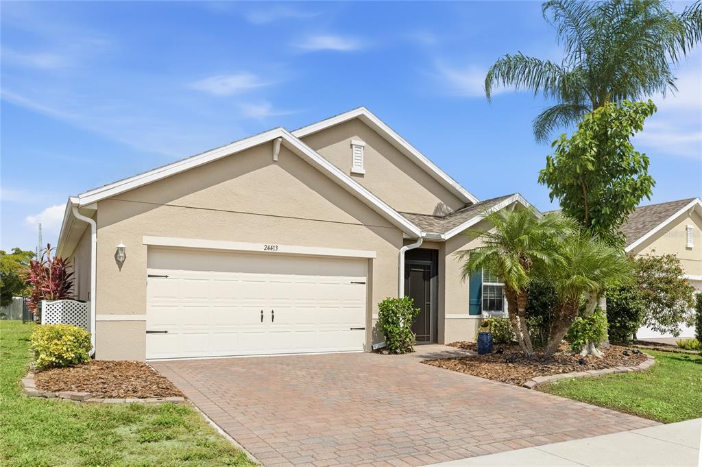 A single-story house with a tan stucco exterior, a two-car garage, and a paver driveway — 24413 BANDONI PLACE, VENICE, FL