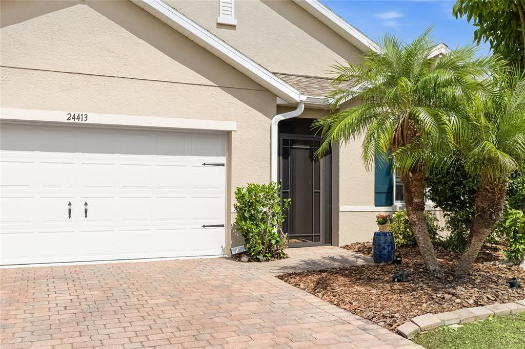 The exterior of a house features a white garage door, a paved driveway, and palm trees — 24413 BANDONI PLACE, VENICE, FL