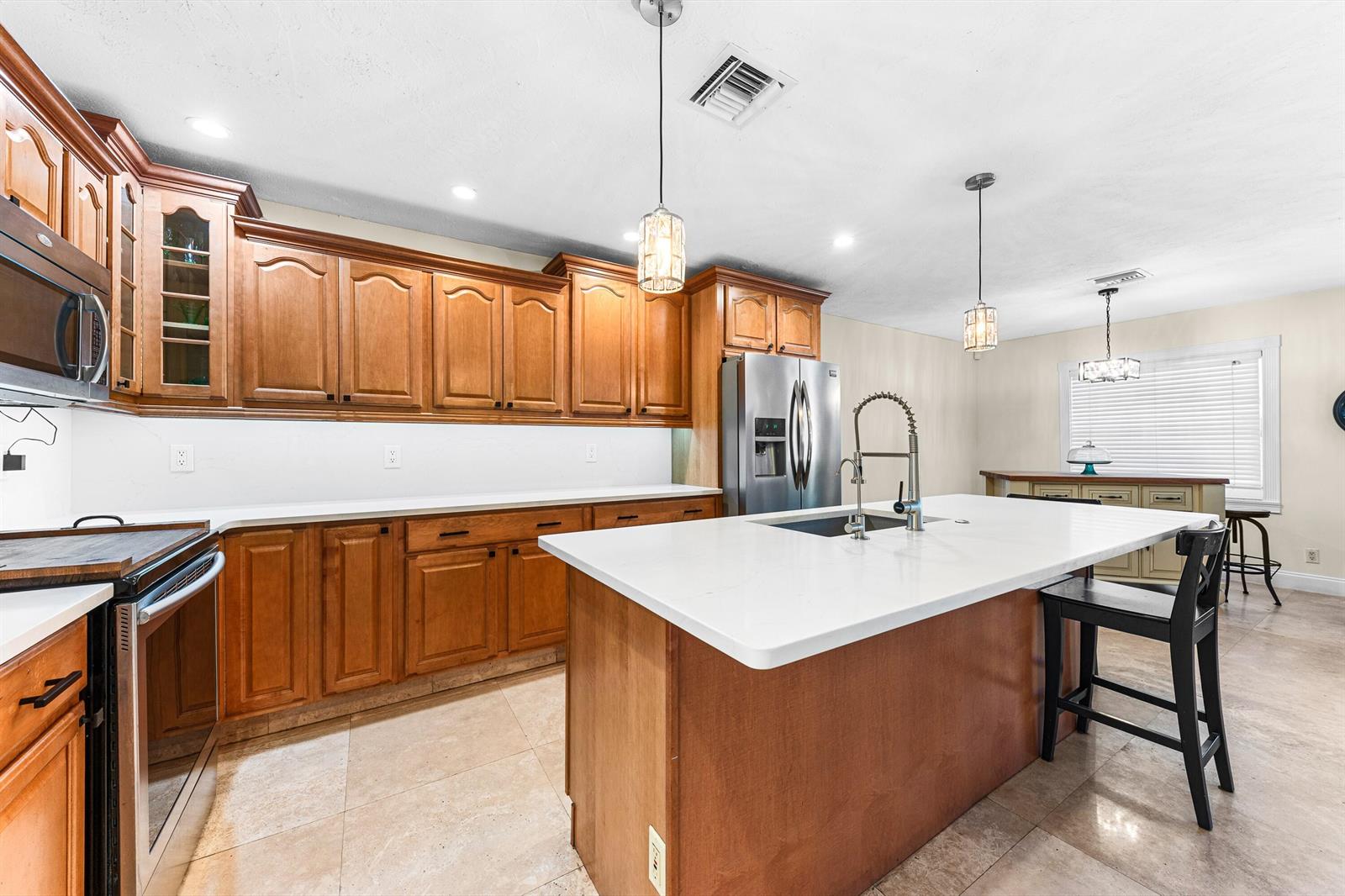 A kitchen features wood cabinets, a white quartz island with a sink, and tile flooring — 6567 Cindi Lane, FL 33467, FL