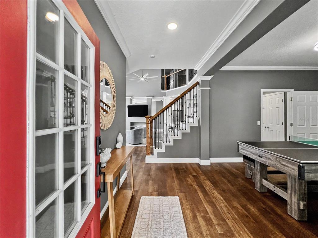 An entryway features a red door, wood flooring, a staircase, and a ping pong table — 1006 SANDLACE COURT, CELEBRATION, FL