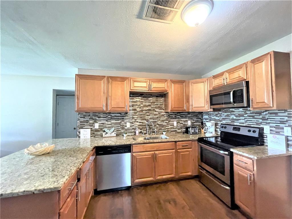 A kitchen features wood cabinets, granite countertops, stainless steel appliances, and a tiled backsplash — 5106 104TH STREET N, ST PETERSBURG, FL