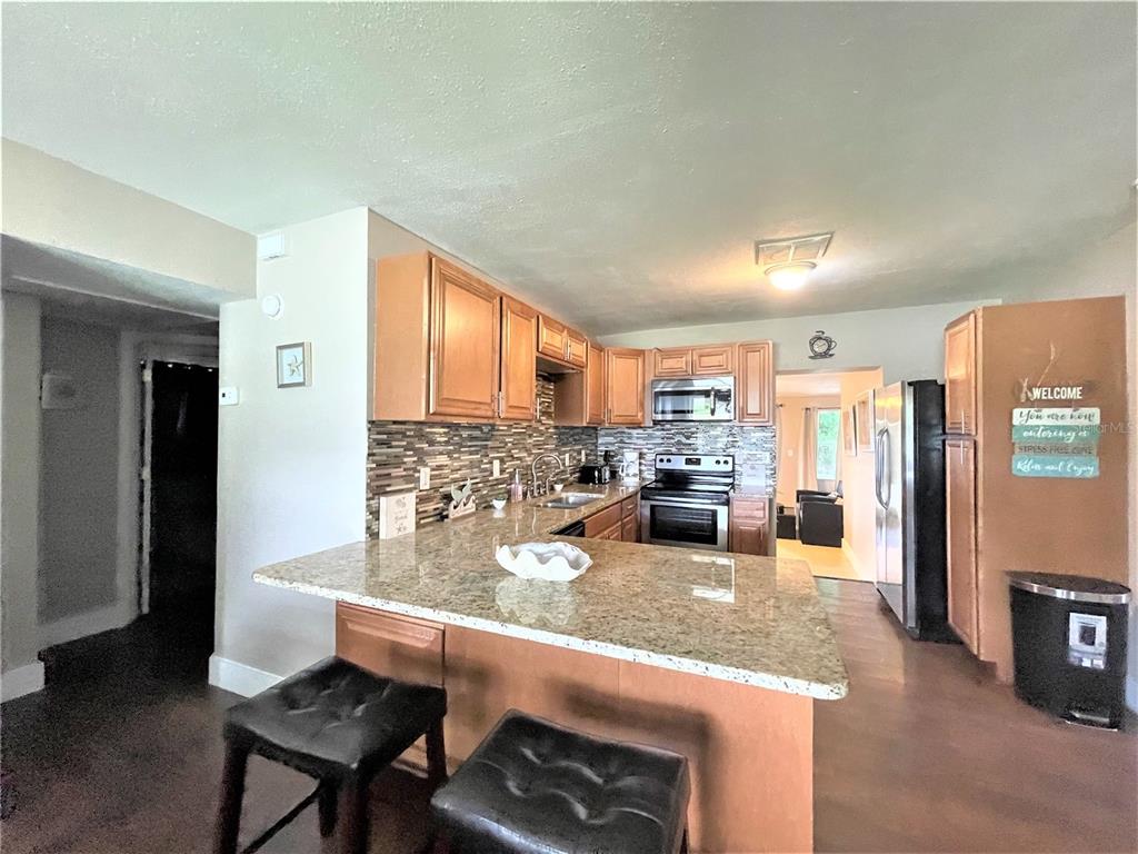 A kitchen features wood cabinets, granite countertops, a breakfast bar, and stainless steel appliances — 5106 104TH STREET N, ST PETERSBURG, FL
