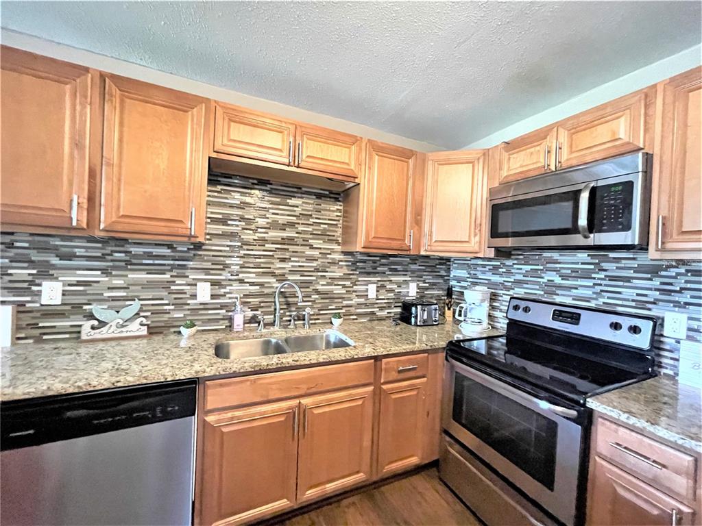 A kitchen features wood cabinets, granite countertops, stainless steel appliances, and a tiled backsplash — 5106 104TH STREET N, ST PETERSBURG, FL