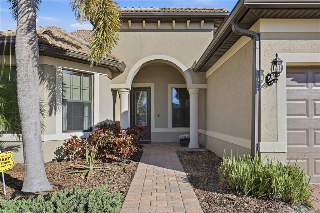 A brick walkway leads to the arched entryway of a house with tan stucco walls — 17203 CORINNA PLACE, LAKEWOOD RANCH, FL