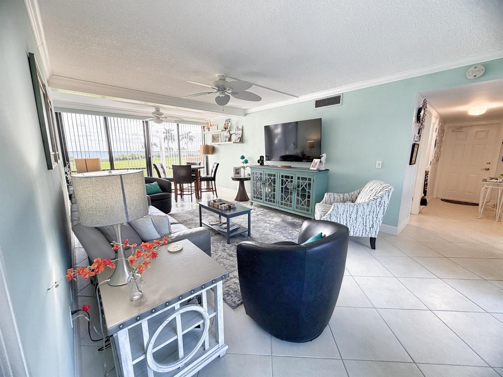 A living room with light blue walls, tile flooring, a television, and a dining area — 3492 NE Causeway Boulevard # 101, Jensen Beach FL 34957, JENSEN BEACH, FL