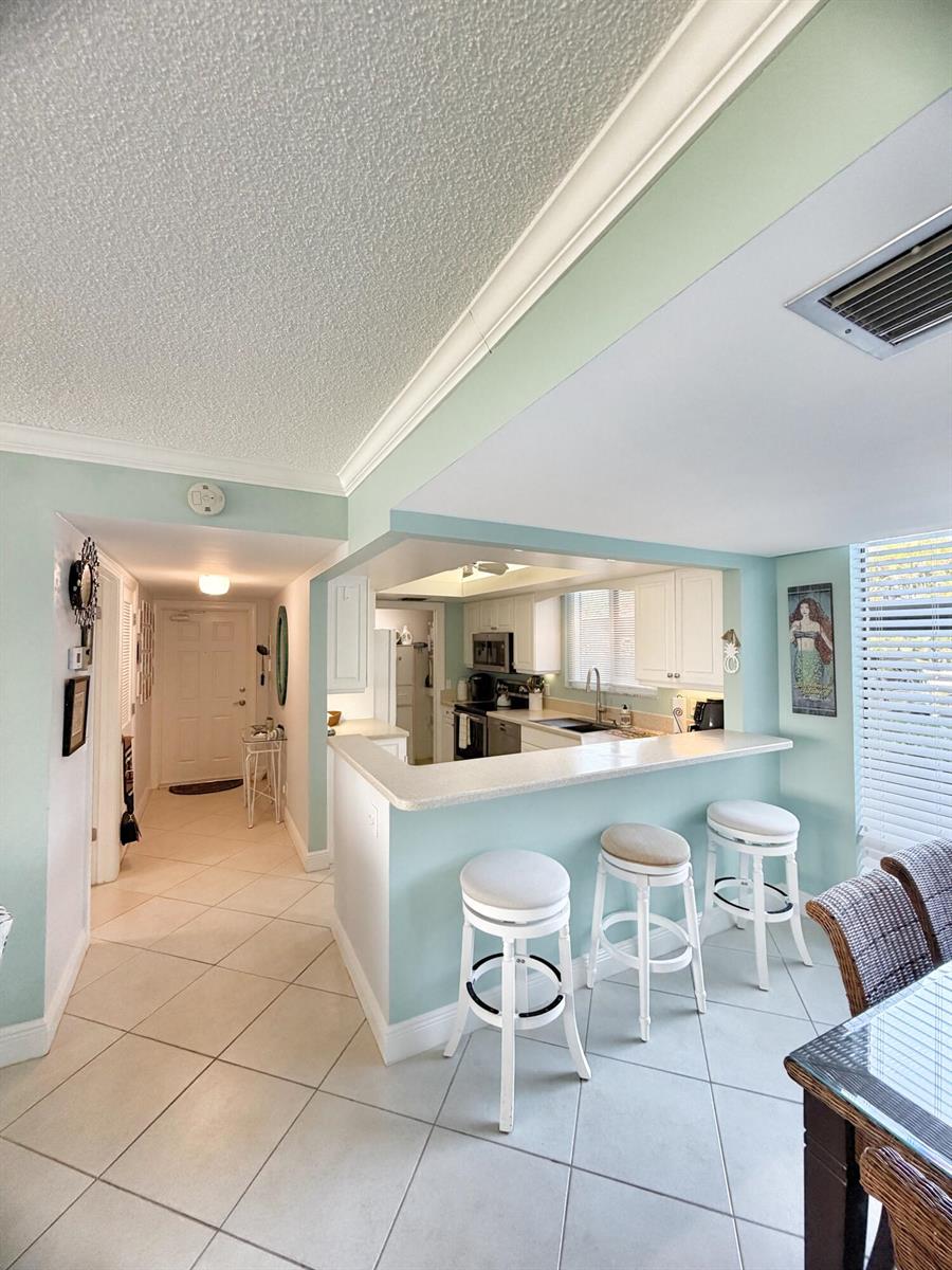 A kitchen with white cabinets and a breakfast bar overlooks a tiled entryway and dining area — 3492 NE Causeway Boulevard # 101, Jensen Beach FL 34957, JENSEN BEACH, FL