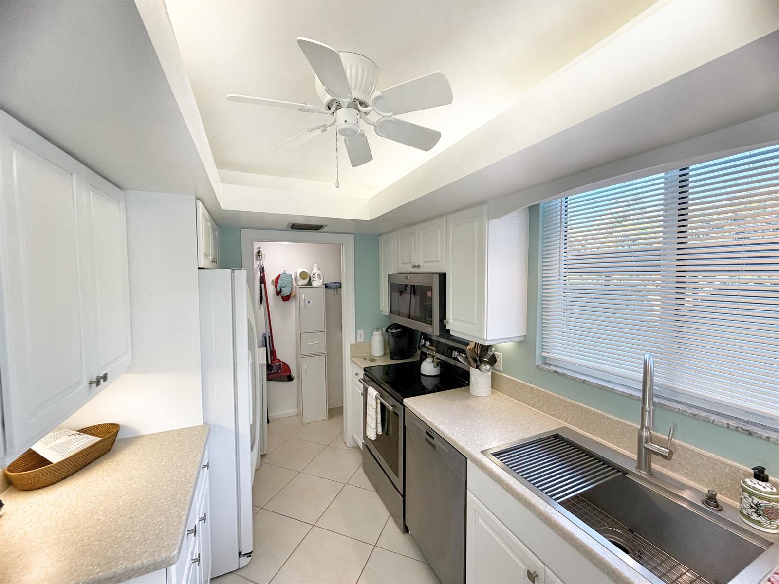 A galley kitchen features white cabinets, stainless steel appliances, a ceiling fan, and tile flooring — 3492 NE Causeway Boulevard # 101, Jensen Beach FL 34957, JENSEN BEACH, FL