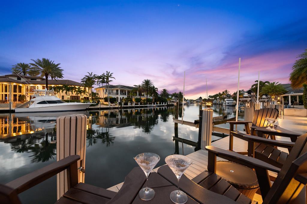 A view from a dock featuring two martini glasses, patio chairs, and docked yachts at sunset — 2600 NE 33rd Street, Lighthouse Point FL 33064, LIGHTHOUSE POINT, FL