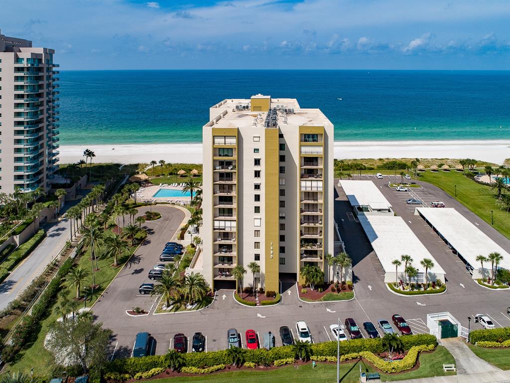 An aerial view shows a multi-story beachfront condominium building with a pool and parking lot — 1480 GULF BOULEVARD UNIT 610, CLEARWATER BEACH, FL