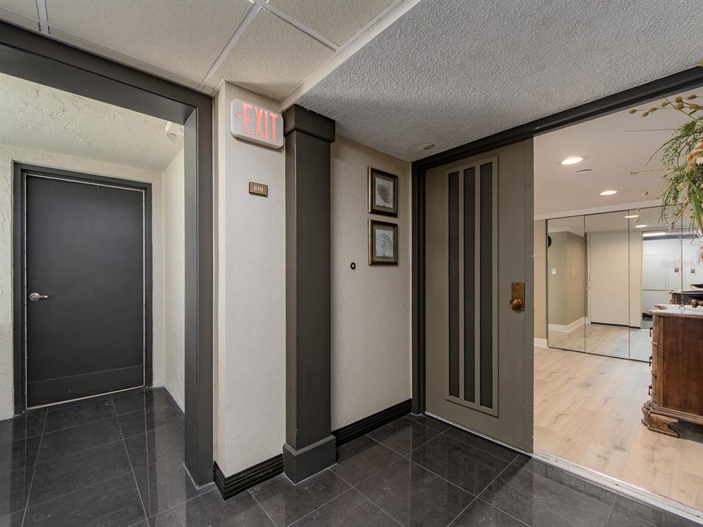 A hallway with dark tile flooring leads to a doorway and a room with mirrors — 1480 GULF BOULEVARD UNIT 610, CLEARWATER BEACH, FL