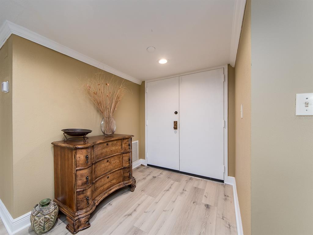An entryway features light wood-look flooring, tan walls, a wooden chest, and double white doors — 1480 GULF BOULEVARD UNIT 610, CLEARWATER BEACH, FL