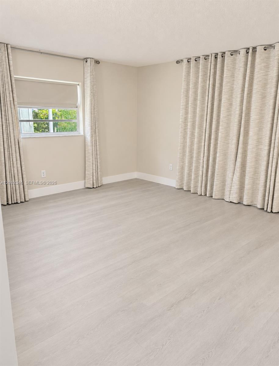 An empty room features light-colored wood-look flooring, beige walls, and floor-to-ceiling curtains — 22745 SW 65th Way # 0, Boca Raton FL 33428, BOCA RATON, FL