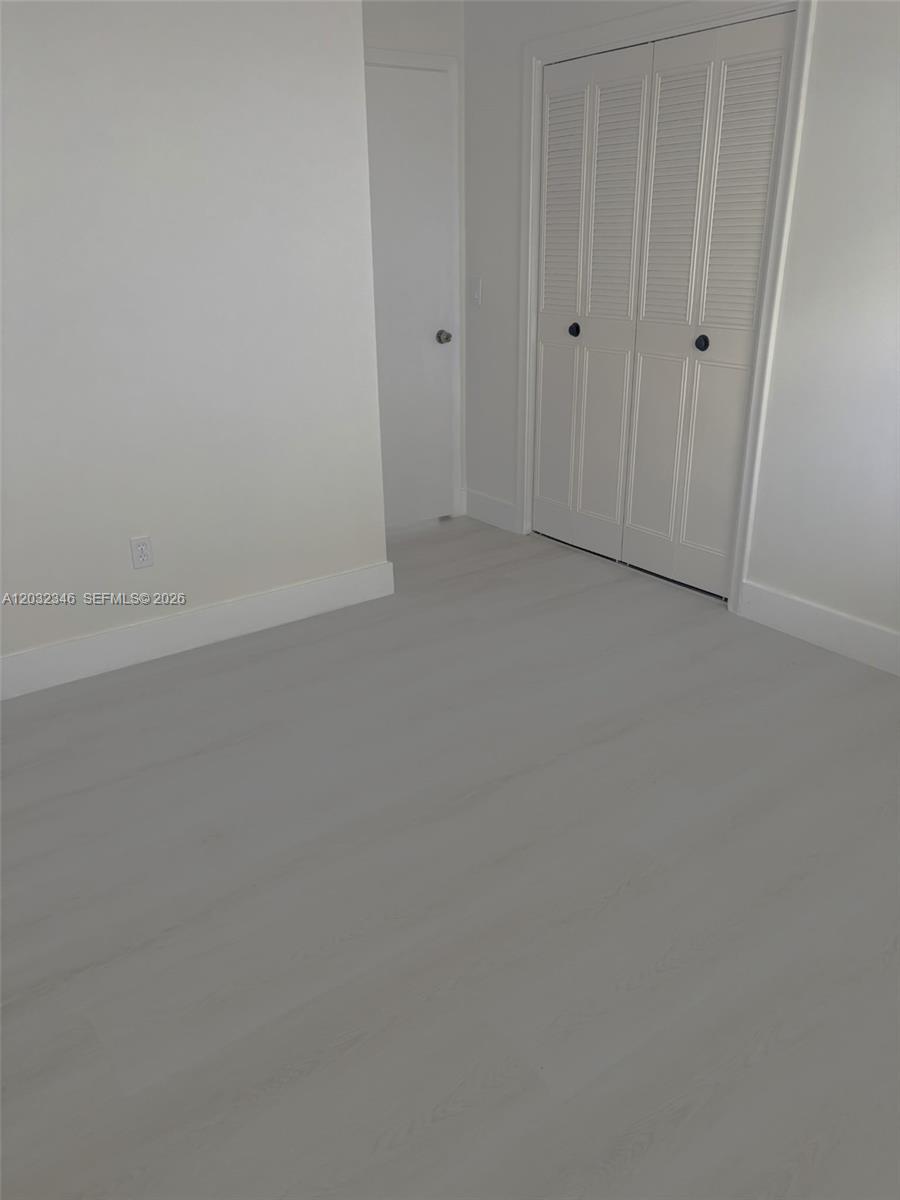 A room with light-colored wood flooring, white walls, a closet with louvered doors, and a door — 22745 SW 65th Way # 0, Boca Raton FL 33428, BOCA RATON, FL