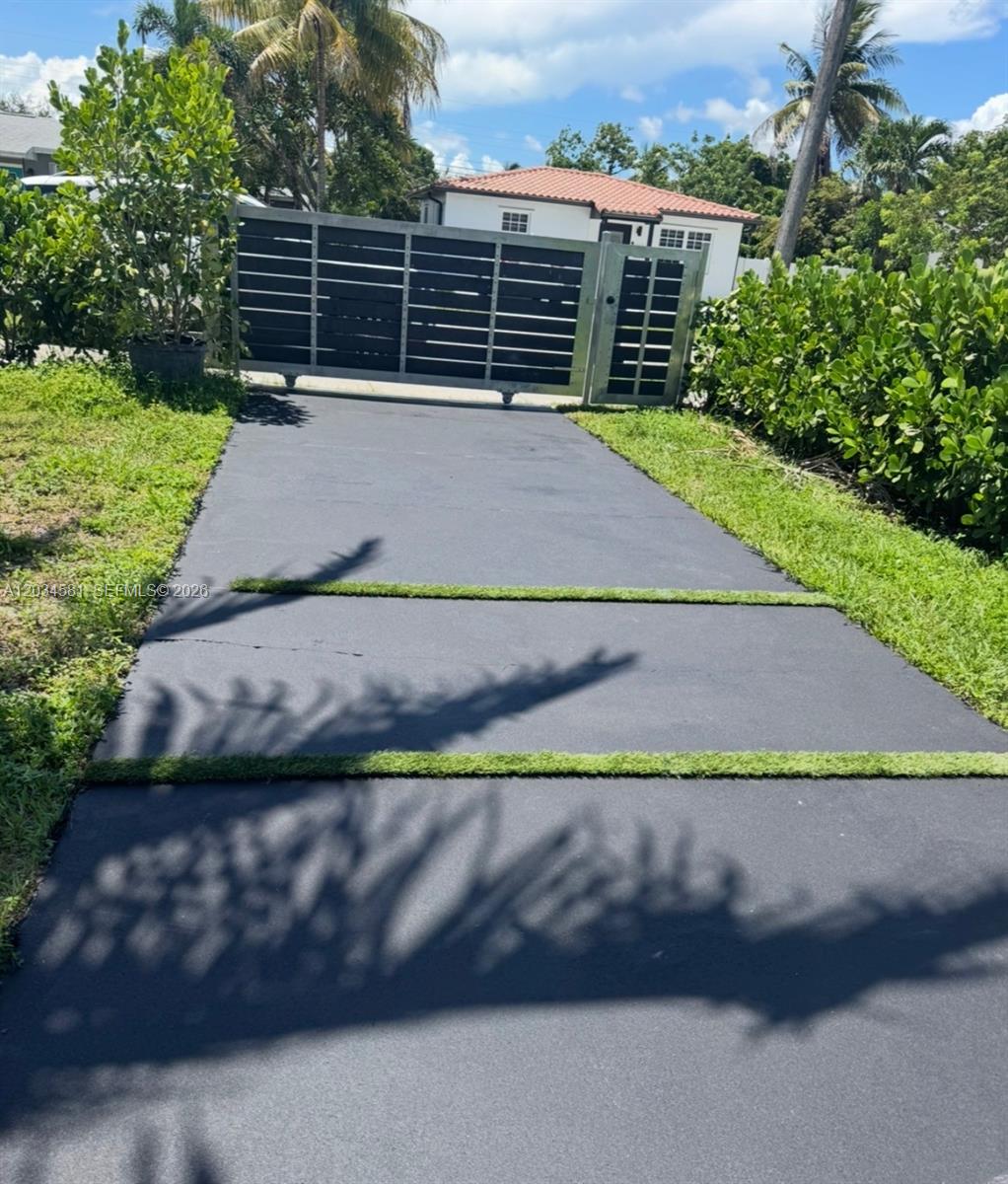 A paved driveway with grass strips leads to a metal gate in front of a house — 2735 Dewey St, Hollywood FL 33020, HOLLYWOOD, FL