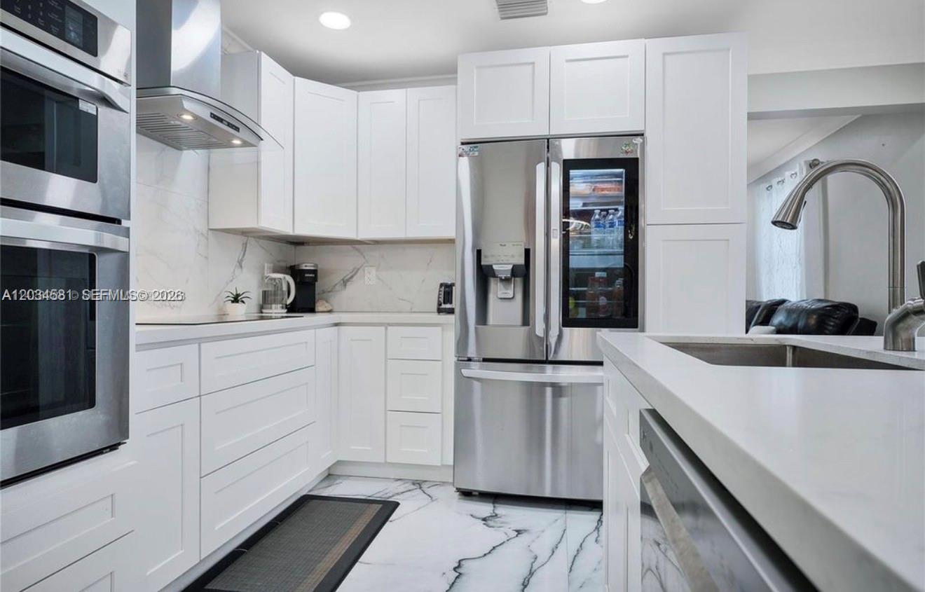 A modern kitchen features white cabinets, stainless steel appliances, and white marble-patterned countertops and flooring — 2735 Dewey St, Hollywood FL 33020, HOLLYWOOD, FL
