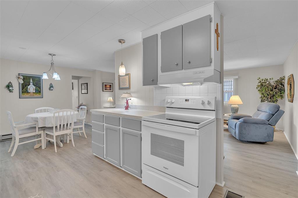 A kitchen with white appliances and grey cabinets opens into a dining area and living room — 5619 BAYSHORE ROAD UNIT 319, PALMETTO, FL