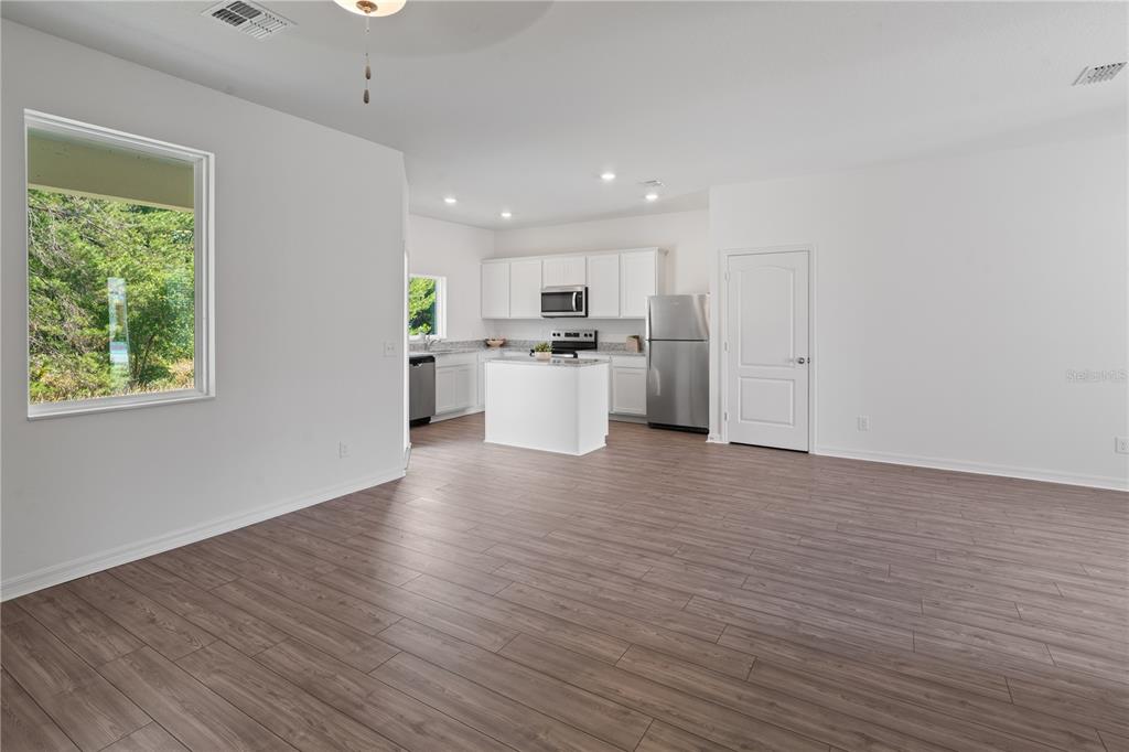 An open-concept kitchen and living area featuring white cabinets, stainless steel appliances, and wood-look flooring — 563 BAY LEAF DRIVE, KISSIMMEE, FL