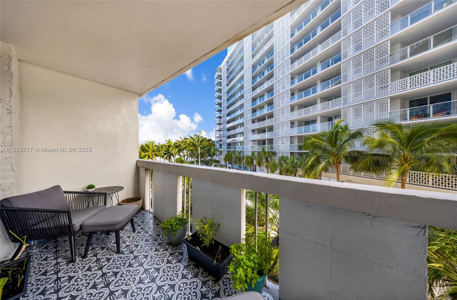A balcony features patterned tile flooring, a lounge chair, and potted plants overlooking a building — 800 West Ave # 338, Miami Beach FL 33139, MIAMI BEACH, FL