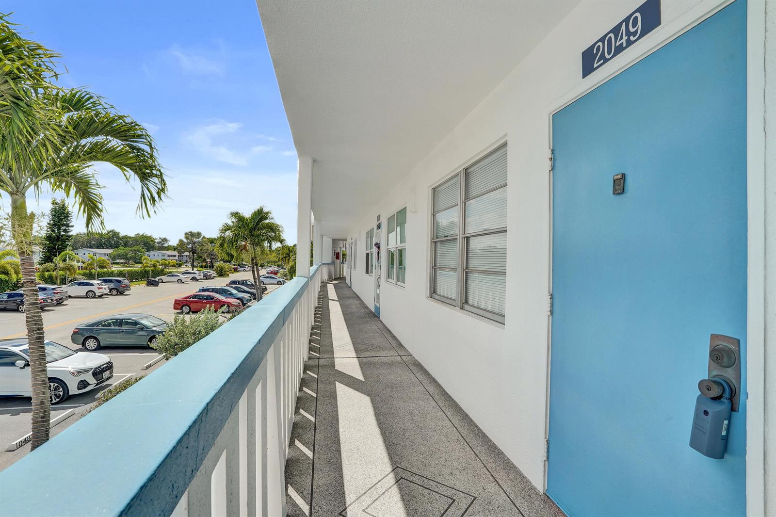 An exterior walkway leads past a blue door marked 2049 toward a parking lot — 2049 Lyndhurst, Deerfield Beach FL 33442, DEERFIELD BEACH, FL
