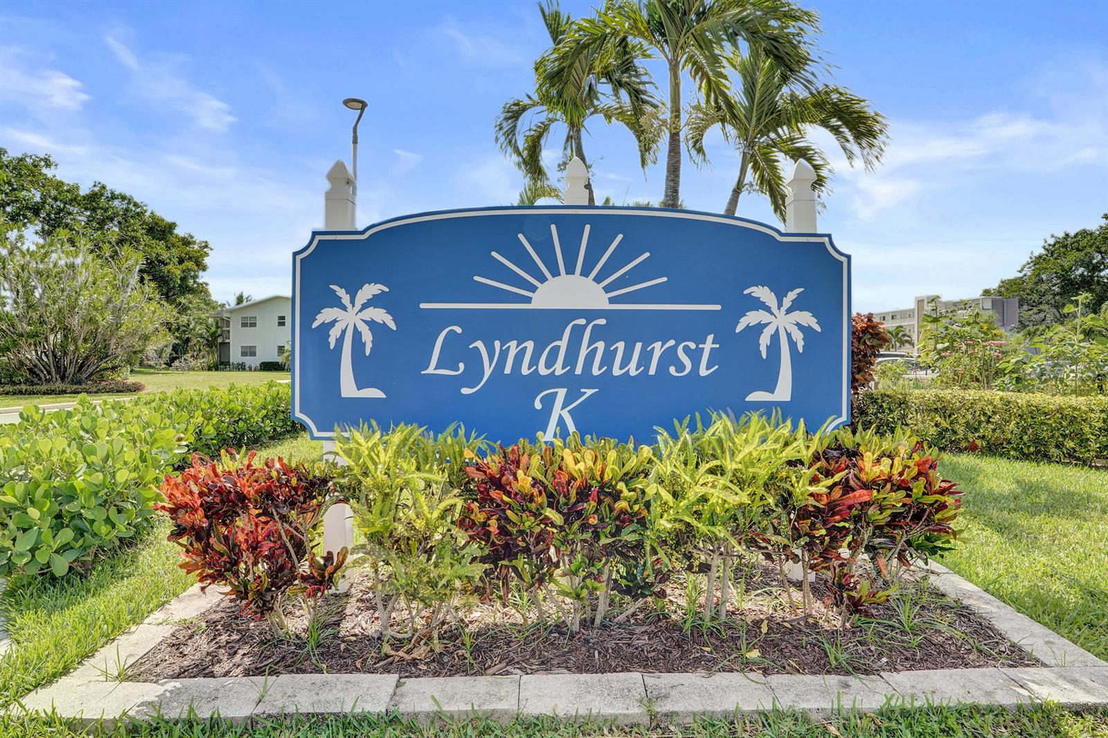 A blue sign with the name Lyndhurst K stands in a landscaped garden area — 2049 Lyndhurst, Deerfield Beach FL 33442, DEERFIELD BEACH, FL