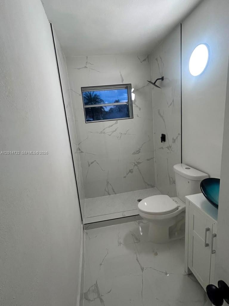 A small bathroom features white marble-look tile, a walk-in shower, and a pedestal sink — 19360 NW 1st Ct, Miami Gardens FL 33169, MIAMI GARDENS, FL