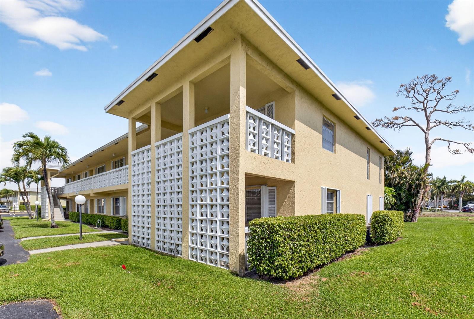 A two-story apartment building features yellow stucco walls and decorative white concrete breeze block screens — 1150 Mahogany Way # 203, Delray Beach FL 33445, DELRAY BEACH, FL