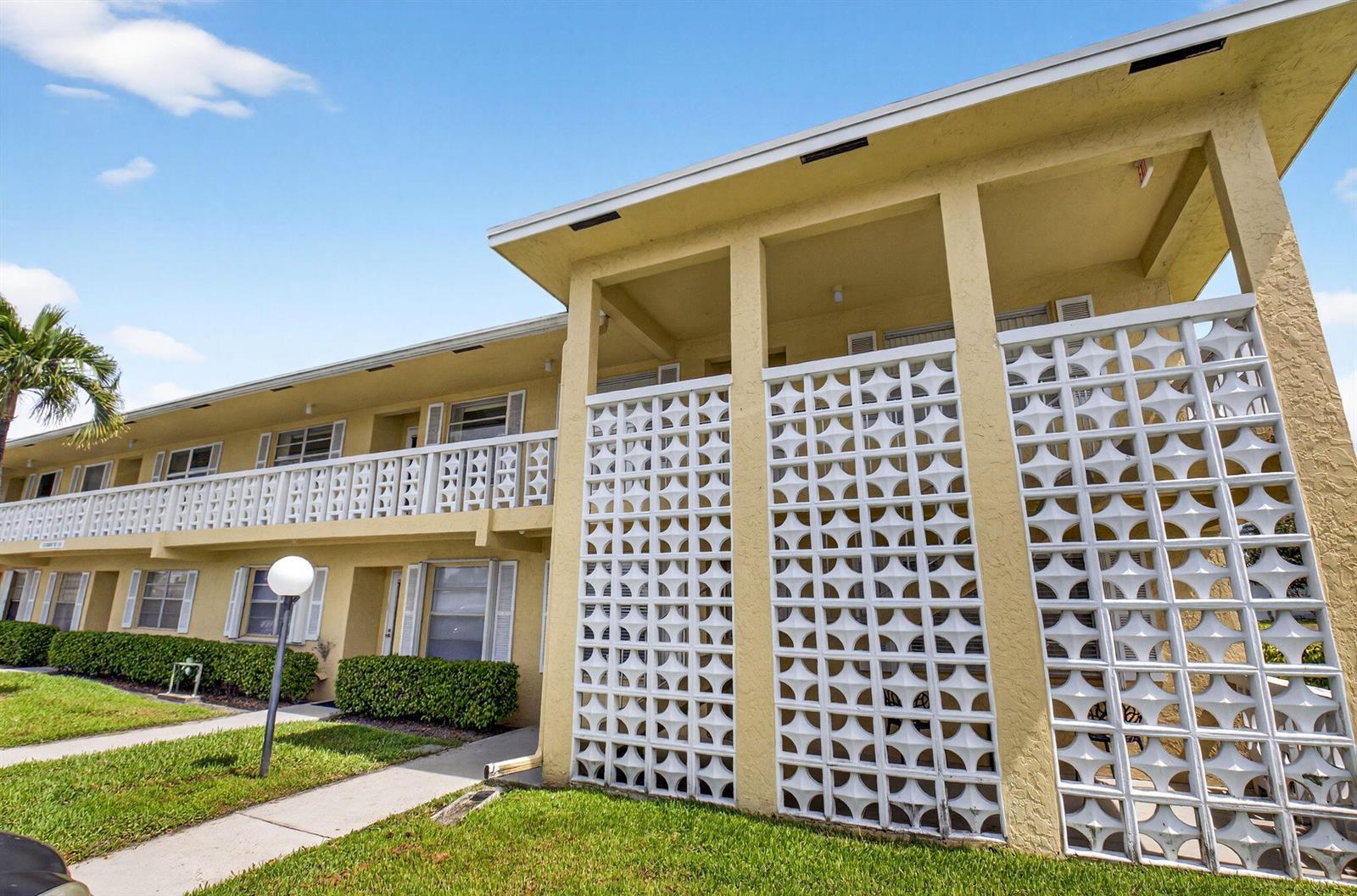 A two-story yellow apartment building features white decorative breeze block privacy screens on the balconies — 1150 Mahogany Way # 203, Delray Beach FL 33445, DELRAY BEACH, FL