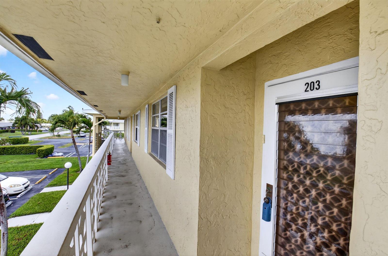 An exterior walkway leads to the entrance of unit 203 with a patterned glass door — 1150 Mahogany Way # 203, Delray Beach FL 33445, DELRAY BEACH, FL