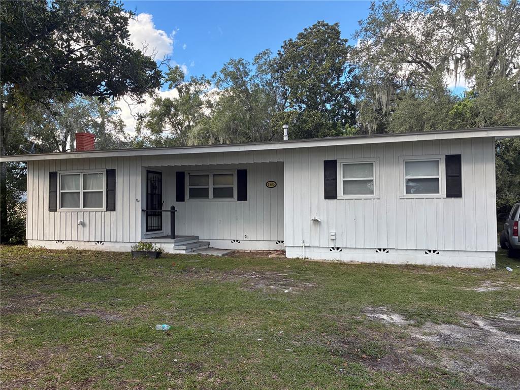 A single-story white house with vertical siding, black shutters, and a recessed front porch — 1905 EMMETT STREET, KISSIMMEE, FL